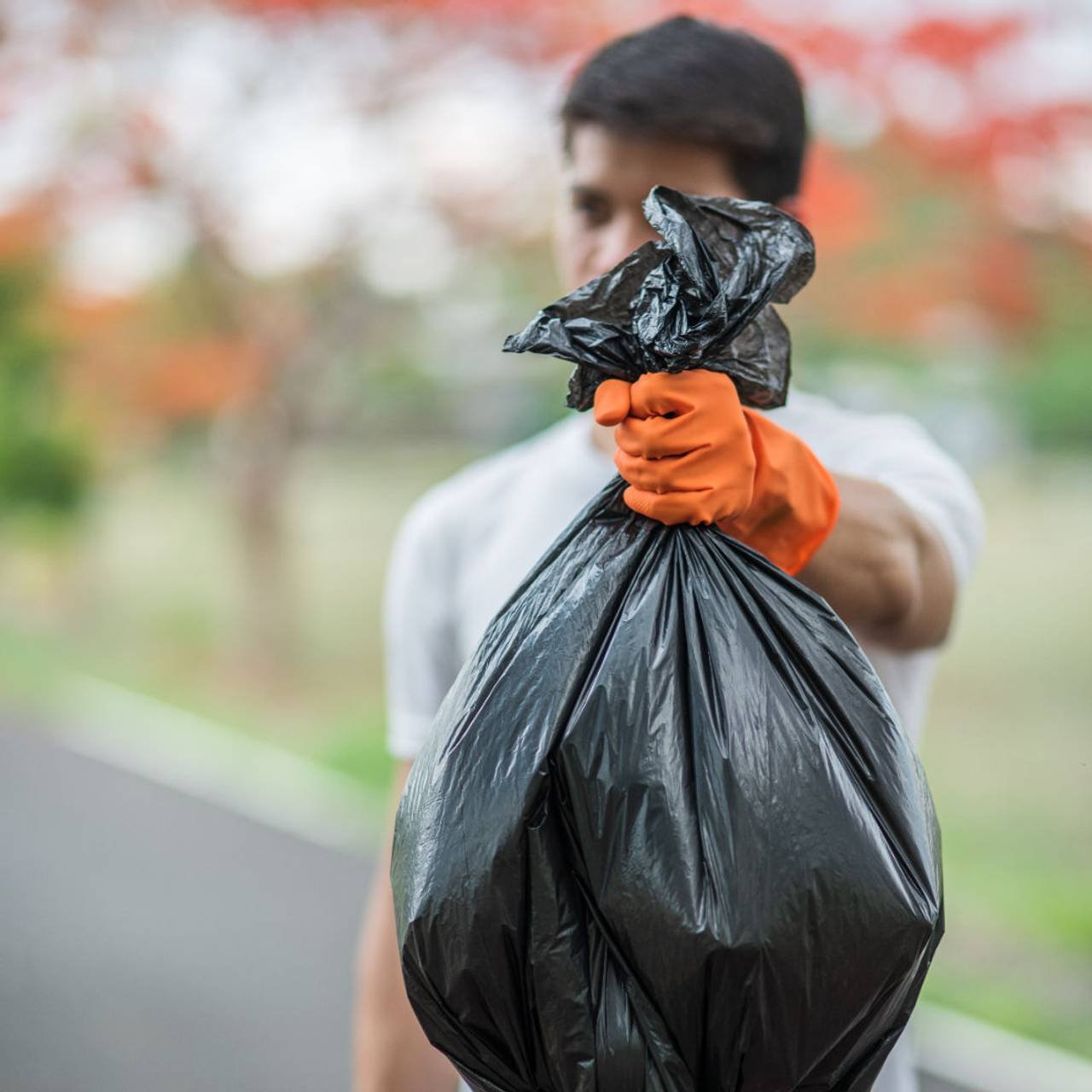 homem usando luvas laranja coletando saco preto de lixo