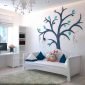 Decoração neutra de quarto de criança com berço-cama branco, almofadas coloridas e desenho de árvore na parede