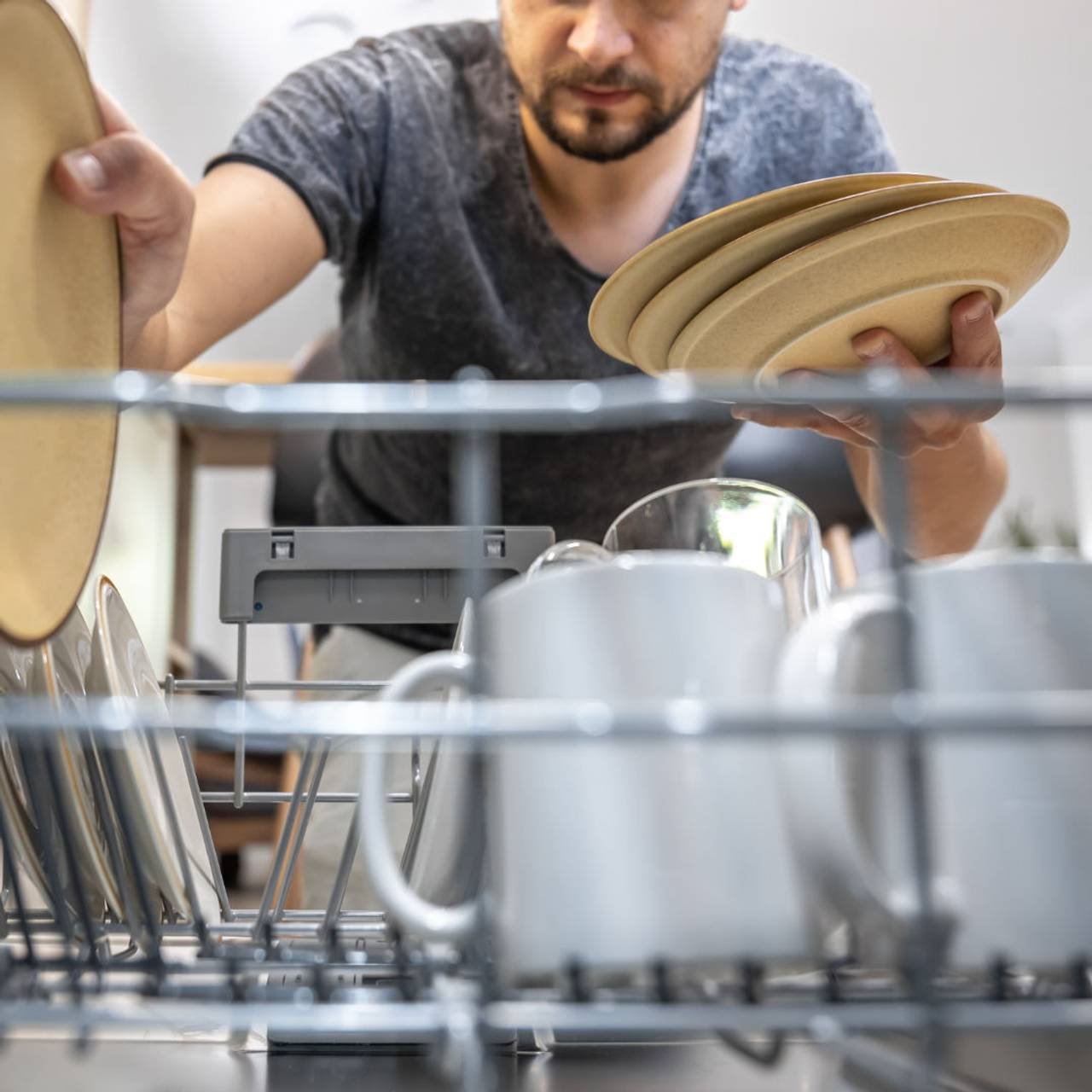 um homem na frente de uma maquina de lavar louca tira pratos limpos apos a lavagem