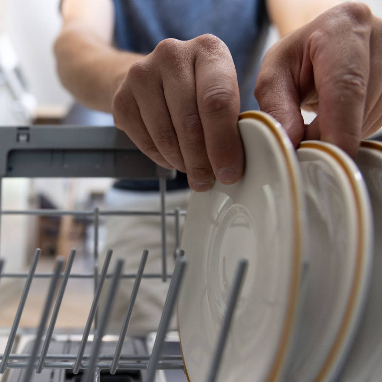 um homem na frente de uma maquina de lavar louca tira pratos limpos apos a lavagem 