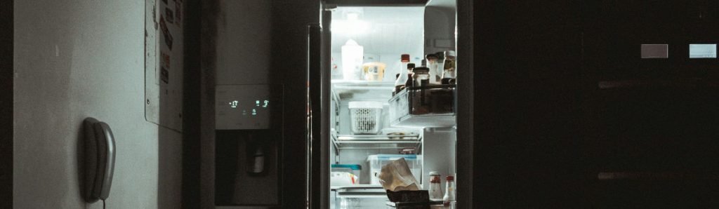 Geladeira de duas portas com apenas um lado aberto e alimentos diversos à mostra