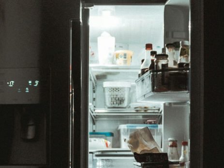 Geladeira de duas portas com apenas um lado aberto e alimentos diversos à mostra