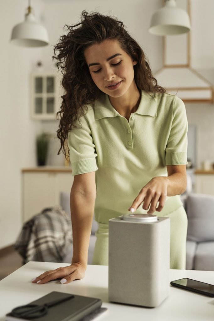 medium shot woman with smart speaker Mulher ajustando um dispositivo em mesa moderna