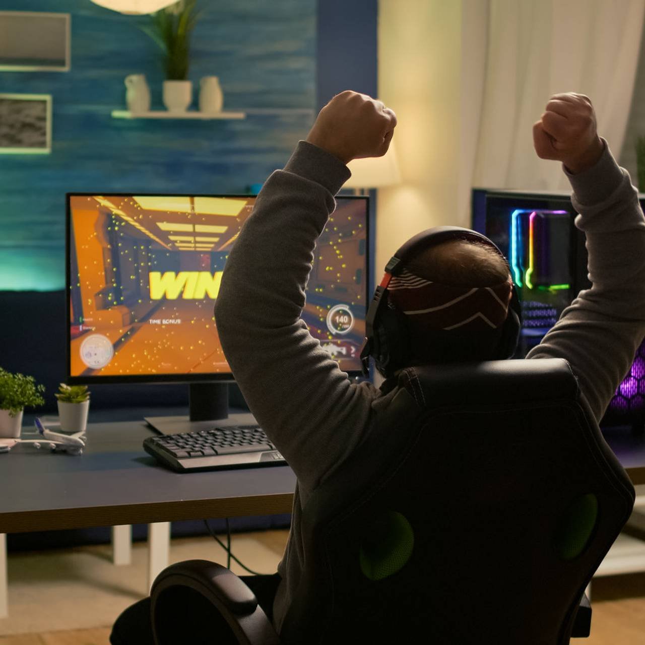 videogamer player raising hands after winning first person shooter competition wearing hradphones professional pro gamer playing online video games with new graphics powerful computer (1)