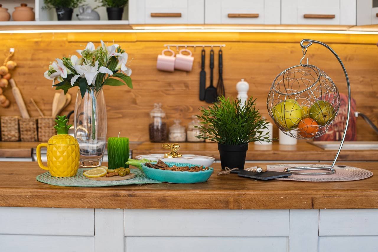 imagem da grande cozinha bem iluminada com armarios brancos e marrons com chaleira de abacaxi amarela moinho de pimenta branca e metal pendurado com frutas e biscoitos