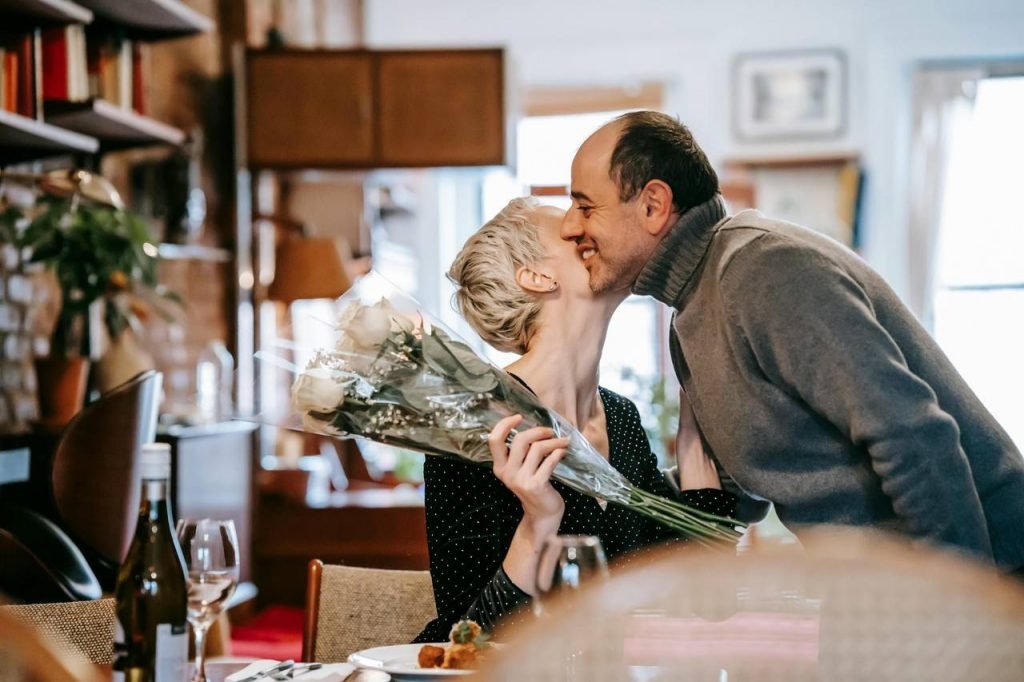 Homem presenteando sua namorada com um buquê de flores e a cumprimentando com um beijo no rosto