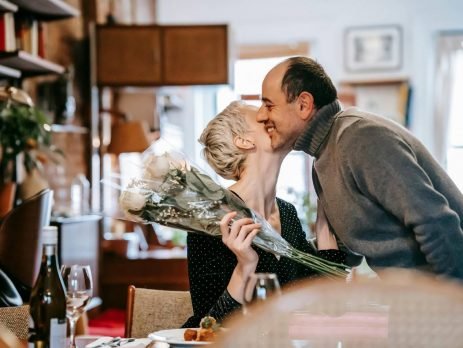 Homem presenteando sua namorada com um buquê de flores e a cumprimentando com um beijo no rosto