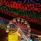 Festa Junina à noite com bandeiras coloridas, barraquinhas de comida, roda gigante e muitas pessoas