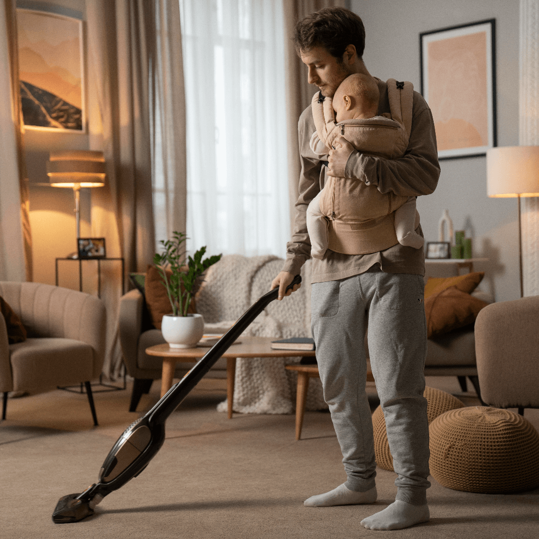 Homem com bebe no colo aspirando a sala de estar
