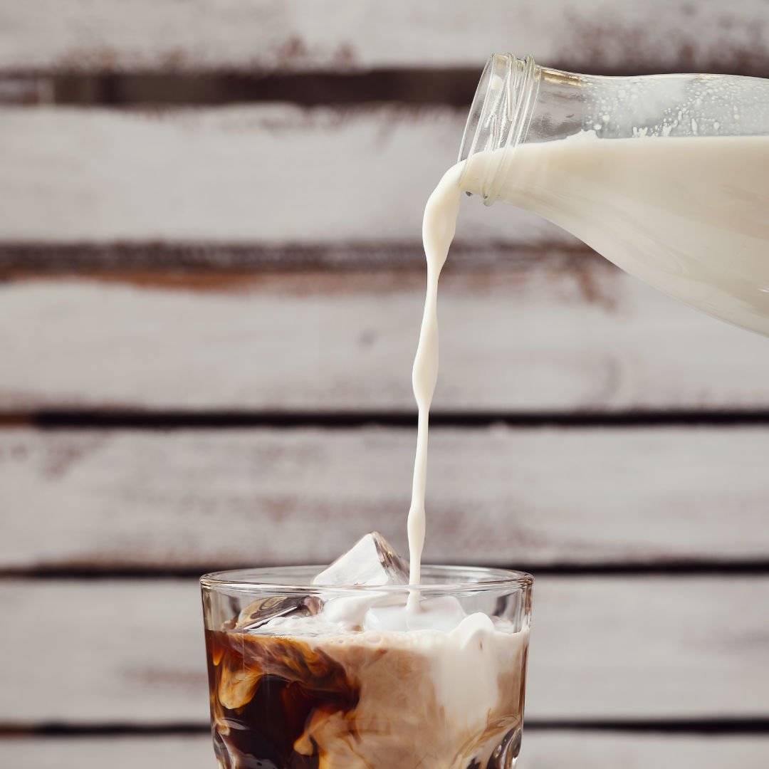 garrada derramanda leite em copo de vidro com café gelado