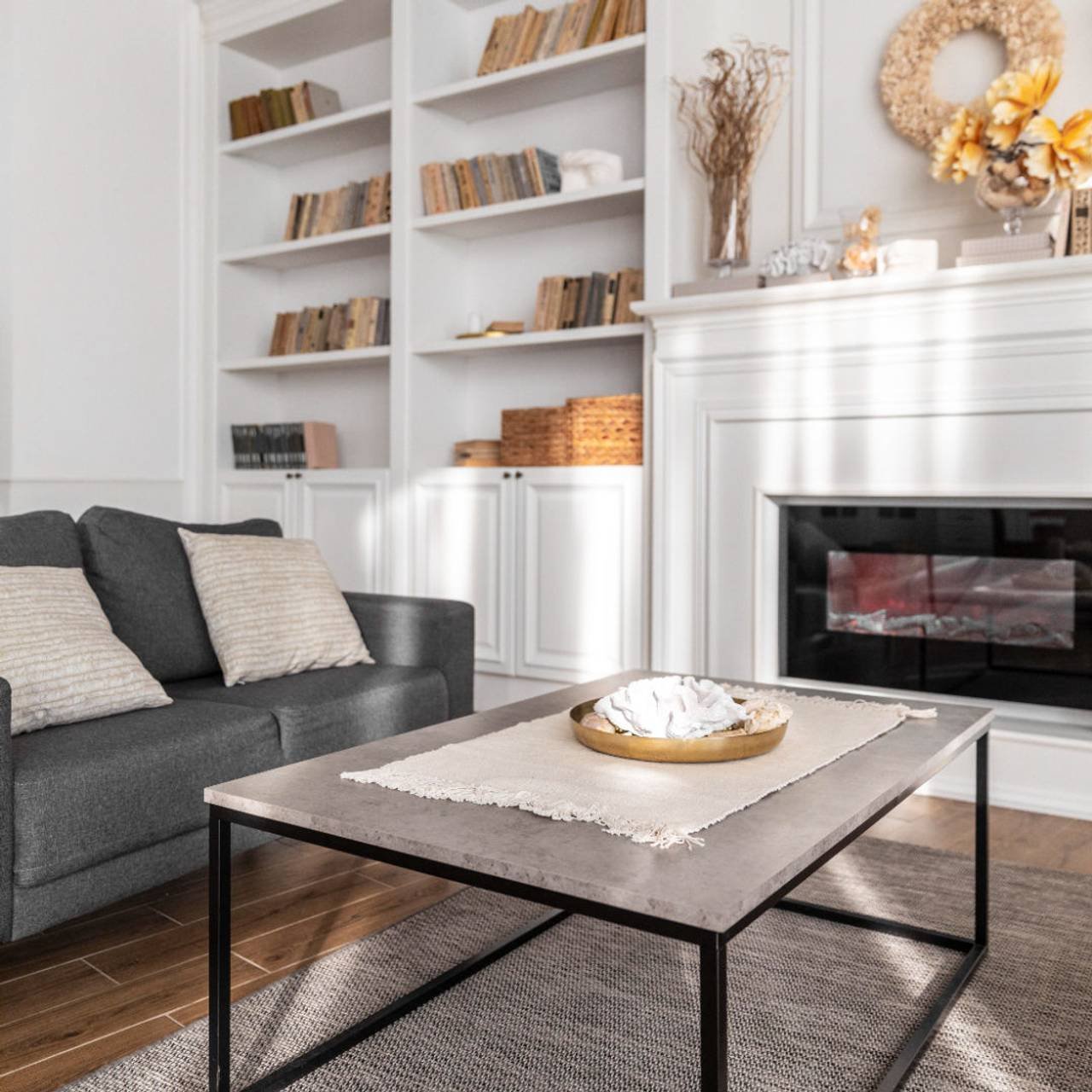Sala de estar com sofá cinza, mesa de centro, lareira e armario branco 