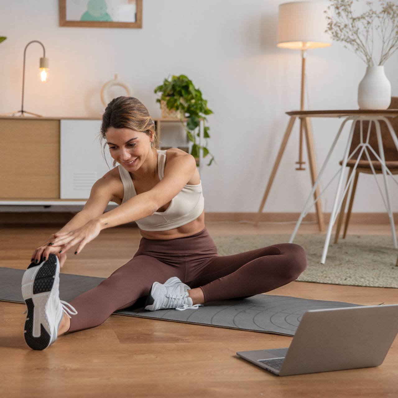 mulher se alongando no chão de sua casa com notebook a frente 