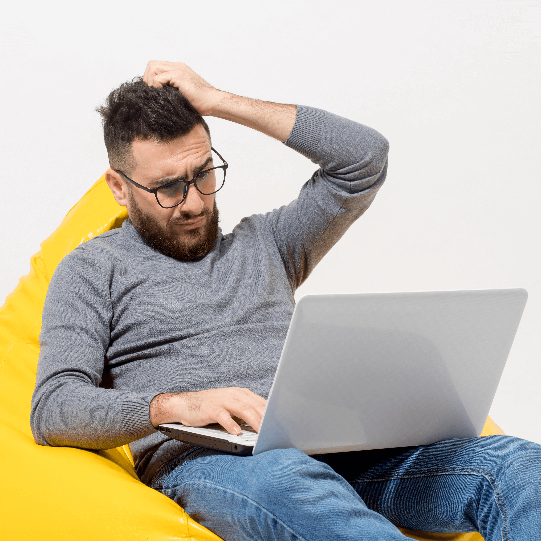 homem pensando deitado em puff amarelo com notebook no colo