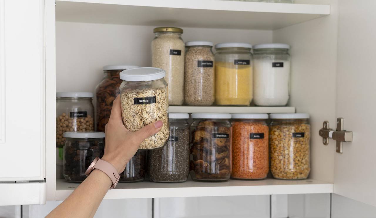 mão segurando jarra de vidro com aveia para guardá-la no armário da cozinha