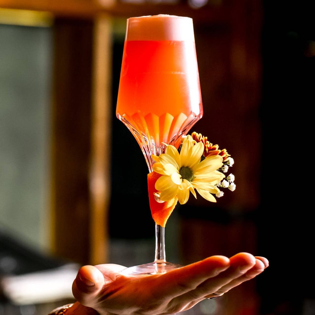homem segura um copo de cocktail de laranja decorado com flor