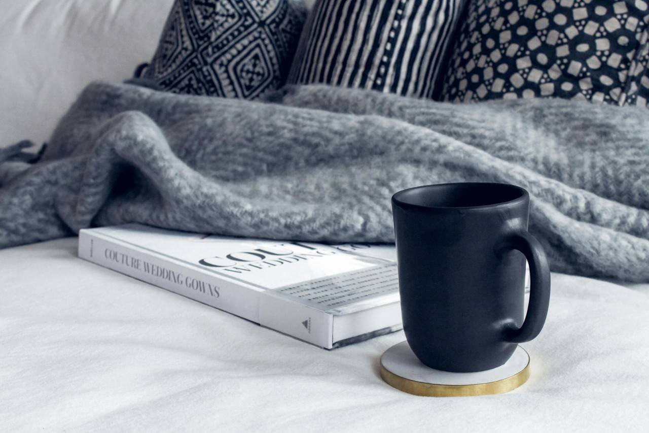 uma xicara preta e um livro sob uma cama com coberta