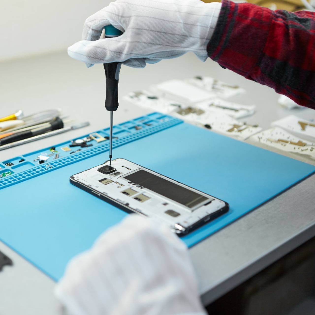 técnico luvas antiestáticas usando chave de fenda desmontar telefone celular borken indo consertar placa-mãe sentado em seu local de trabalho laboratório com o equipamento necessário