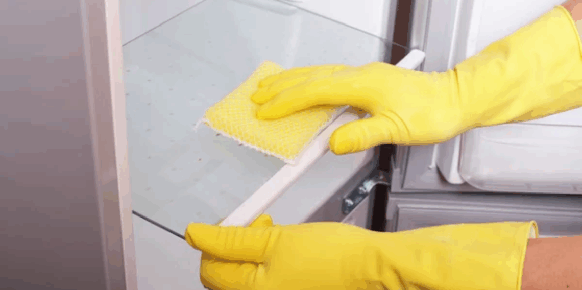 Pessoa limpando prateleira de geladeira com esponja